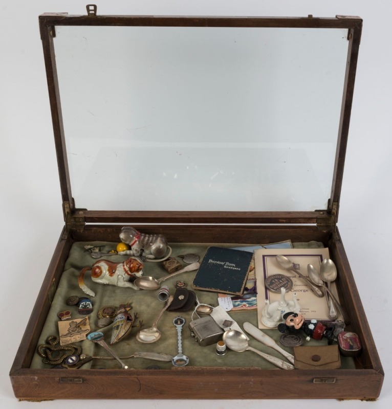 A glass-top display case with various items including an Australian 1938 Crown, several clockwork toys, spoons, badges, etc. 37 x 51 x 7.5cm.