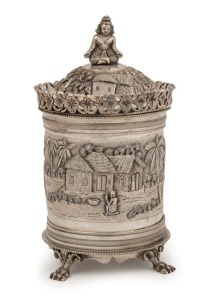 An antique Indian silver tea caddy with ornate village scene decoration, lion's paw feet and seated figural finial, 19th/20th century, 14.5cm high, 276 grams
