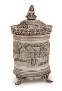 An antique Indian silver tea caddy with ornate village scene decoration, lion's paw feet and seated figural finial, 19th/20th century, ​​​​​​​14.5cm high, 276 grams
