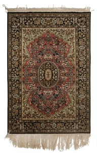 A Persian hand-knotted silk rug with ornate floral motif with black, olive and terracotta ground, 172cm x 112cm