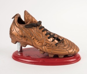 A match-worn gold Adidas football boot mounted on a stand; signed by several noted players including Tommy Hafey, Ron Barassi, Kevin Sheedy. Probably bought at a charity event.