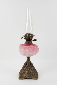 An antique oil lamp with gilded cast metal base, pink glass font, black button double burner and glass chimney, 19th century, 60cm high