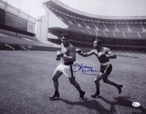 KEN NORTON signed photograph depicting him playfully chasing Muhammad Ali around Yankee Stadium prior to their fight in September 1976. Overall 28 x 35.5cm with CofA.