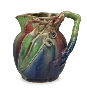 REMUED pottery jug with applied gumnuts, branch handle and leaf, glazed in pink, blue and green, incised "Remued", 15cm high