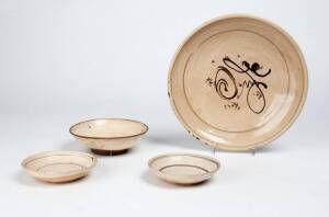 A large Cizhou dish with Fu character in the centre in iron brown, 25cm diameter and three small Cizhou dishes, all Ming Dynasty, 14.8cm, 11.5cm diameter