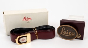 LEITZ: Two Leica-branded clothing items - one leather belt and one brass belt buckle, both in their original Leica-branded boxes. (2 items)