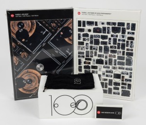 LEITZ: Five '100 Years of Leica Photography' commemorative items, including two sealed jigsaw puzzles, one animation flipbook, one point of sale camera display, and one felt pouch. (5 items)