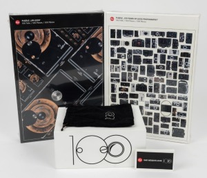 LEITZ: Five '100 Years of Leica Photography' commemorative items, including two sealed jigsaw puzzles, one animation flipbook, one point of sale camera display, and one felt pouch. (5 items)