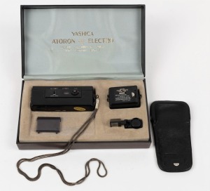 YASHICA: 1970 Atoron Electro subminiature camera [#30700496] with Yashinon 18mm f2.8 lens, presented in original wooden laminate box with lens cap, flash unit, angle viewfinder, wrist chain, leather case, and cleaning cloth.