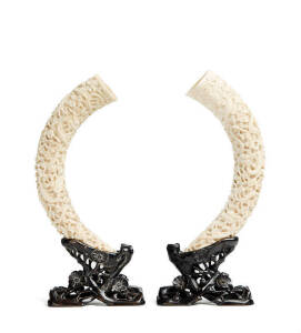 A pair of Chinese ivory tusks, carved with dragons, fitted and carved wooden stand, early 20th century, 29cm and 28.5cm long
