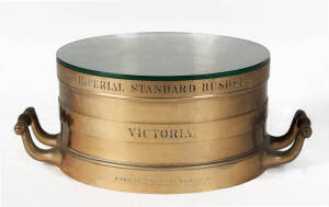 A large brass two handle grain measure, inscribed 'Imperial Standard Bushell Victoria', fitted with a glass top, 25.5cm high, 47.5cm diameter