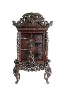 A Japanese lacquered wood display cabinet, early 20th century, surmounted by an impressive pediment depicting a dragon and two phoenix, supported on a separate base with a deeply carved apron of exotic flowers, 216cm high, 116cm wide and 57cm deep