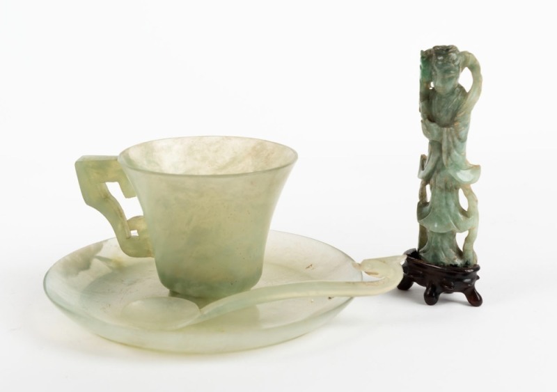 Chinese jade cup, saucer and spoon; together with a Chinese carved jade statue on a carved wooden stand, 19th/20th century, (4 items), ​​​​​​​the statue 8cm high.