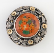 RHODA WAGER (attributed) circular silver brooch with gold highlights, set with a hand-painted floral porcelain panel signed "A.V." on the reverse. Purported to be the work of artist AMY VALE. 3.5cm wide