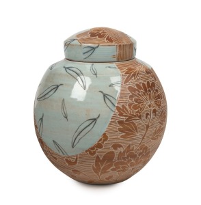 JANET De BOOS brown glazed lidded pottery vase, adorned with sgraffito decoration and hand-painted gum leaves in gloss blue, 22cm high, 19cm wide