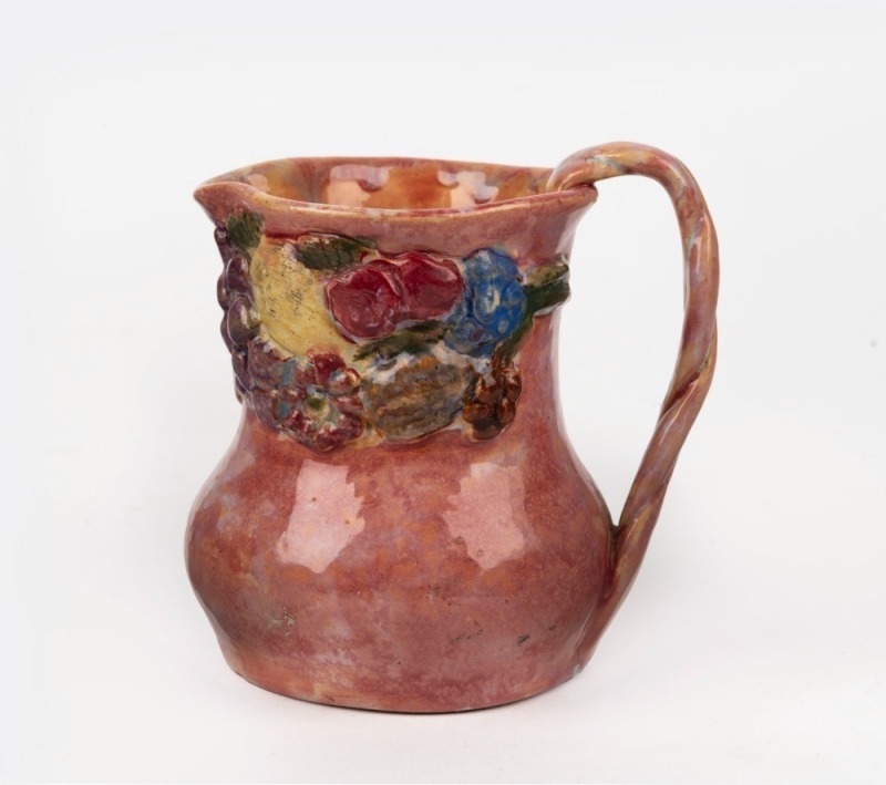 UNA DEERBON pink glazed pottery jug with applied fruit decoration, incised "Deerbon", 11.5cm high