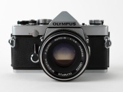 OLYMPUS: 1972 chrome-body Olympus M-1 SLR camera [#135685] with M-System Auto-S 50mm f1.8 lens [#125174]. Very few of these cameras and lenses were produced before name was&nbsp;changed to 'OM-1' to avoid infringing on the Leitz&nbsp;M1 trademark. - 2