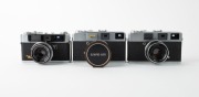 OLYMPUS: Three late 1950s rangefinder cameras - one Olympus Auto [#108199] with G. Zuiko 42mm f1.8 lens [#108605] and Olympus Auto metal lens hood, one Olympus Auto B [#102879] with E. Zuiko 42mm f2.8 lens [#102669], and one Olympus Auto Eye [#113895] wit - 2
