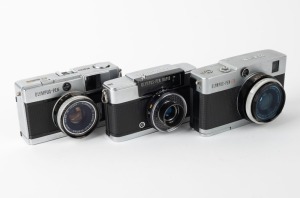 OLYMPUS: Three c. 1967 35mm half-frame cameras - one Pen-EM [#105763] with F. Zuiko 35mm f2 lens and Olympus 82C lens filter, one Pen Rapid-EE S [#100335] with D. Zuiko 30mm f2.8 lens and Olympus lens hood, and one Pen-EED [#251516] with F. Zuiko 32mm f1.