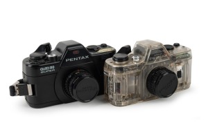 ASAHI KOGAKU: Two 110-cartridge SLR cameras - one c. 1979 Pentax Auto 110 with clear plastic body together with Pentax-110 24mm f2.8 lens [#1295813] and front lens cap, and one c. 1982 black-body Pentax Auto 110 Super with Pentax-110 24mm f2.8 lens [#1132