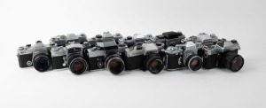 VARIOUS MANUFACTURERS: Eleven black-and-chrome SLR cameras - one Foto-Quelle Revueflex SL 301, one Ihagee Exakta RTL 1000, one Kamera Werkstätten Praktica VLC2, one Mamiya/Sekor 500 DTL, one Minolta SR-1 with front lens cap, one Minolta SRT-101 with front lens cap, one Miranda Sensorex, one Olympus FTL, one Tokyo Kogaku Topcon IC-1, one Yashica Electro AX, and one Wirgin Edixa Reflex. (11 cameras)