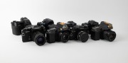VARIOUS MANUFACTURERS: Eight black SLR cameras - one Canon PowerShot Pro1 with lens hood and lens cap, one Konica Minolta Dynax 5D with lens hood, one Minolta Maxxum 7000 AF with front lens cap, one Olympus Camedia E-10, one Ricoh KR-10, one Voigtl&auml;nder V