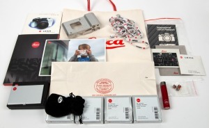 LEITZ: Twenty-one Leica promotional items - one unpainted Leica T aluminium body housing, three Leica lanyards with 'Red-Dot' logo, one red Leitz cigarette lighter, four Leica '100 Years' pin badges in felt pouches with maker's boxes, three Leica 'Red-Dot' pin badges, one aluminium bank card holder in maker's box, one Leica shopping bag, one Leica R8 promotional CD-ROM in digipack case, and others. (21 items)