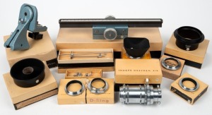 IHAGEE: Twelve accessories in individual maker's boxes - one 210mm focusing rack, one steel camera cradle with rotating head, one type 1 shutter release bridge, one type 2 shutter release bridge, two lens reversing rings with differing diameters, one Exakta 49mm lens hood, two lens hood extension elements, one 50mm D-ring adapter, one type 2 adapter ring for microscope connection, and one set of three lens extension tube lengths. (12 items)