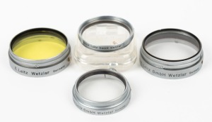 LEITZ: Four different chrome lens filters - one XOOQG yellow, one XOOYL UV, one HOOIV UVa in maker's plastic case, and one FIOLA UVa. (4 items)