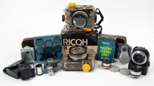 RIKEN: Eleven Ricoh accessories, some in maker's boxes - two Marine AD underwater housings, one AF Rikenon 50mm f2 lens, one aux telephoto lens for 45mm f2.8 with cap, one aux wide-angle lens for 45mm f2.8 with cap, one finder for aux lens, one TC-9 Tele Conversion Lens in maker's leather case, one Sindo Ricoh set of five lens filters plus holder in plastic carry case, one BC-605D flash unit with leather case, sync cable, and instruction booklet, and two other flash units. (11 items)