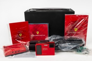 OLYMPUS: Ferrari Digital Model 2004 digital camera [#07561], in lined black maker's box with leather case, charging stand, strap, software CD, various charging and data cables, and printed matter.