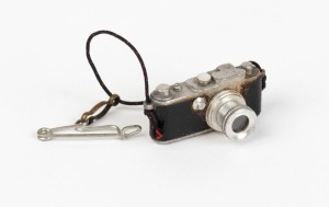 LEITZ: Extremely rare 23x13x14mm stanhope microphotograph viewer in shape of Leica camera, featuring photograph of the Leitz factory in Wetzlar. These were pinned as souvenirs to the lapels of visitors to the Leitz exhibit at the first camera Photokina trade fair, held in Cologne in 1950.