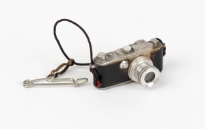 LEITZ: Extremely rare 23x13x14mm stanhope microphotograph viewer in shape of Leica camera, featuring photograph of the Leitz factory in Wetzlar. These were pinned as souvenirs to the lapels of visitors to the Leitz exhibit at the first camera Photokina tr