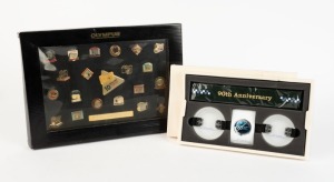 OLYMPUS: Commemorative '10 Million Sold' framed sales retrospective set of twenty-one pins depicting many famous camera models and gold plaque thanking Michaels Camera Video & Digital, together with black protective sleeve. Also one 90th Anniversary Olympus Space Project Commemorative Kit comprising two replicas of the Olympus E-3 lens caps designed for use on the International Space Station, with camera strap and information sheet in maker's box. (2 items)