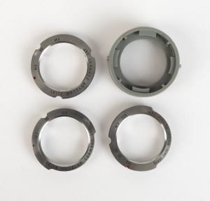 LEITZ: Four c. 1950s Leica M lens attachments - one ISOOZ adapter for 135mm, two ISBOO adapters for 90mm, and one type 2 grey plastic lens coupling ring. (4 items)