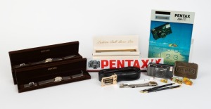 ASAHI KOGAKU: Twenty-three Pentax-branded items, including six Hong Kong-made quartz wristwatches in silver and gold, five of them in presentation boxes, together with three ball-point pens in black and gold, two ball-point pens in white and gold, five different Pentax product pins, one Pentax Zoom-70 jumbo calculator, one belt, one belt buckle, and other items. (23 items)