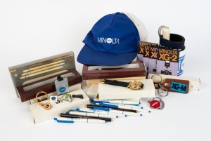 MINOLTA: Thirty-nine Minolta-branded items, including four boxed gold quartz wristwatches, seven metal ball-point pens (four of them in presentation boxes), ten plastic ball-point pens, four keyrings, two tie-clips, two pins, one mug, two baseball caps, a