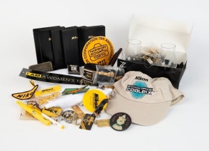 NIPPON KOGAKU: Fifty-three Nikon-branded items, including seventeen pins, seven tie clips, nine keyrings, one belt, one belt buckle, one T-shirt, one hat, two Z-series drinking glasses, one golf tee set, one key wallet, five business diaries, and many oth