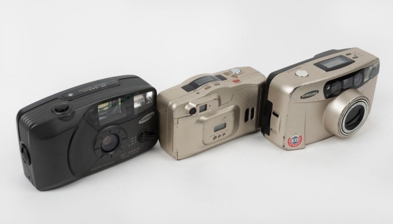 SAMSUNG: Three c. 1999 plastic compact cameras - one Fino 145s in gold, one Maxima Zoom 130 GL in gold, and one AF-444WR in dark grey. (3 cameras)