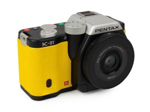 ASAHI KOGAKU: 2012 yellow-body Pentax K-01 digital camera [#4308569], with SMC Pentax-DA XS 40mm f2.8 lens, together with power pack. Camera base bears a print of the signature of Australian industrial designer Marc Newson, responsible for the camera's un