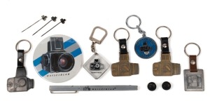 HASSELBLAD: Thirteen Hasselblad-branded items, comprising six metal keyrings, five pins, one badge, and one metal pen with lid. (13 items)