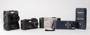 NIPPON KOGAKU: Five c. late 1990s digital cameras showcasing several daring early design choices - one Coolpix 100, one Coolpix 300 with unusual coupled touchscreen PDA and voice memo feature, one Coolpix 900, one Coolpix 5000 with coupled MB-E5000 battery pack/grip, and one Coolpix 800. Maker's box/pouch/cables are present for Coolpix 300. (5 items)
