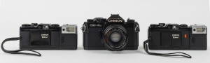 CHINON: Three c. 1980 35mm cameras - one CM-4s SLR with Auto Chinon 50mm f1.9 lens [#752977], together with two Bellami compact cameras [#237164 & #184665], both with wrist straps and with one maker's box/instruction booklet/case present. (3 cameras)