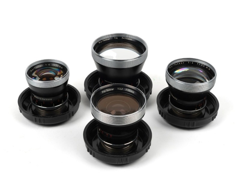 CARL ZEISS: Four c. 1950s Contaflex Pro-Tessar lenses in plastic domes with  front lens caps - one 35mm f3.2 [#4684189], one 35mm f4 [#2357491], one  85mm f4 [#1878081], and one 115mm f4 [#3981570]. (4 items)