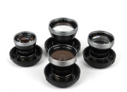 CARL ZEISS: Four c. 1950s Contaflex&nbsp;Pro-Tessar lenses in plastic domes with front lens caps - one 35mm f3.2 [#4684189], one 35mm f4 [#2357491], one 85mm f4 [#1878081], and one 115mm f4 [#3981570]. (4 items)