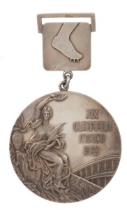 MEXICO CITY 1968 SUMMER OLYMPICS GOLD WINNER'S MEDAL The Mexico Gold Medal awarded to Australia's Maureen Caird for the 80m HURDLES, gilt silver, 60mm, 125gms, originally designed by Guiseppe Cassioli. The front inscribed "XIX OLIMPIADA MEXICO 1968" and features a "Seated Victory" with the Colosseum in the background; th reverse depicts a victorious athelete with palm branch being carried on the shoulders of other athletes. A small plaque attached to the top bears a pictogram