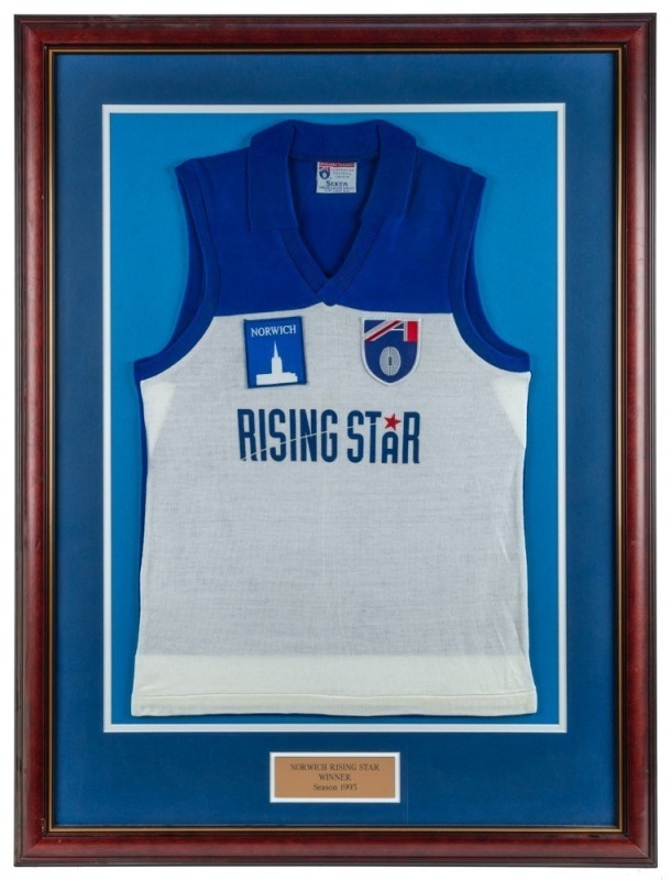 Commemorative ‘Rising Star’ guernsey awarded to Nathan Buckley for winning the Norwich Rising Star award in 1993. Blue and white jumper with AFL and Norwich logos. Framed & glazed. This was the inaugural year of the Rising Star award, which is given to th