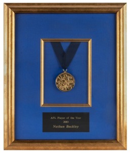 The Lou Richards medal, presented to Nathan Buckley for being judged ‘Player of the Year’ in 2003. The Lou Richards Medal is presented by Channel Nine’s Sunday Footy Show to the player voted by its panellists as the most valuable of the season. Framed & glazed, mounted on blue background.