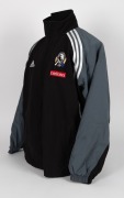 Nathan Buckley’s Collingwood players’ jacket circa 2001-02. Black adidas jacket with full zip, adidas logo on right breast, Collingwood logo on left breast, above small red Emirates patch. Black front with grey sleeves and white striping/highlights. Large - 2