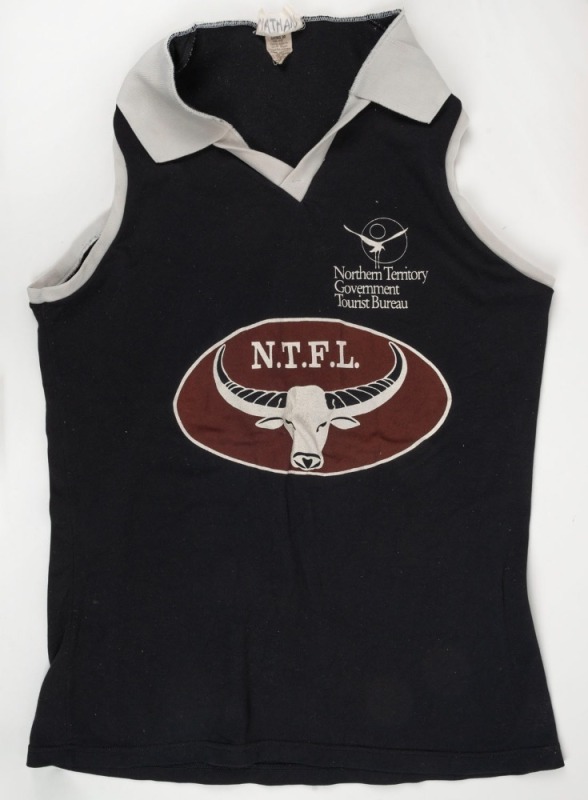 NTFL representative training guernsey, c1992. Black with white collar and edging. Oval NTFL badge in centre of jumper, ochre with steer horns. NT Government Tourist Bureau badging. 2 examples issued to Nathan Buckley.